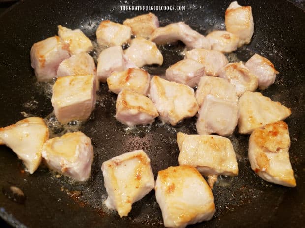 Boneless, skinless chicken breast cubes are lightly browned in hot oil in a skillet.