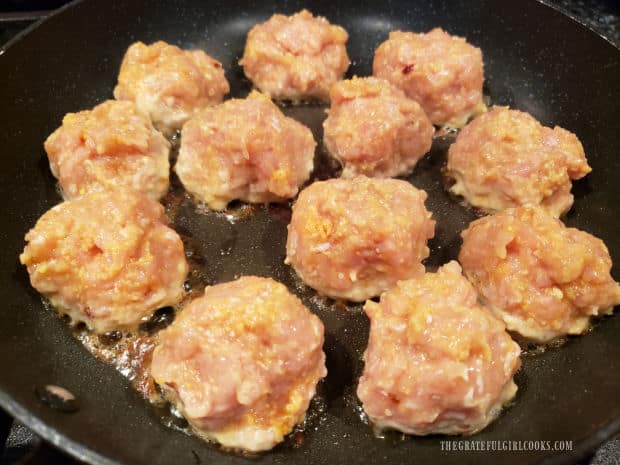 A dozen firecracker chicken meatballs cooking in olive oil in skillet.