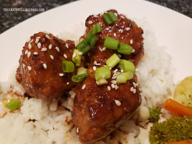 Firecracker chicken meatballs are served on top of white rice, with veggies on the side.