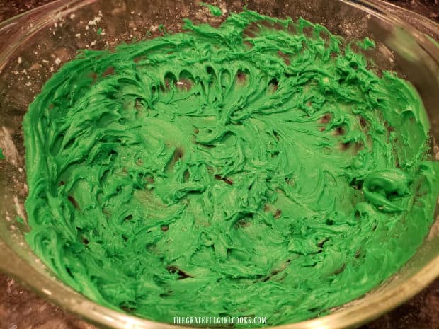 Green peppermint flavored frosting is mixed together in a bowl while cookies bake.
