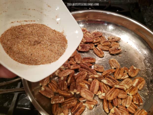 Spices will be added to the oil-coated pecans in the skillet, then stirred to combine.