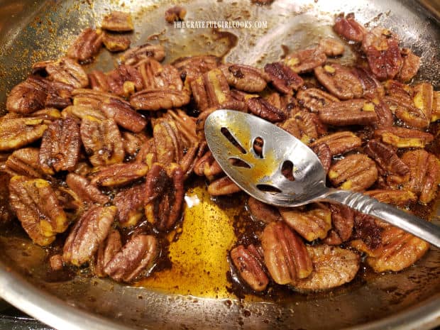 Toasted sweet spiced pecans are removed from the skillet using a slotted spoon.