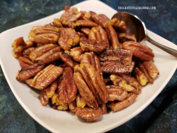 A white bowl, full of toasted sweet spiced pecans ready for snacking.
