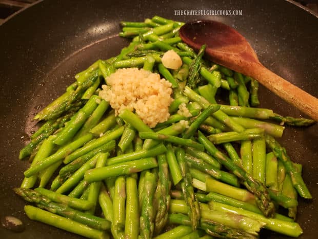 Minced garlic and ginger are added to the cooked asparagus in the skillet.