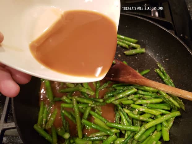 Stir fry sauce is poured into the skillet with the asparagus and cooked until thickened.