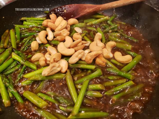 Roasted cashews are added to the asparagus cashew stir fry in the skillet.