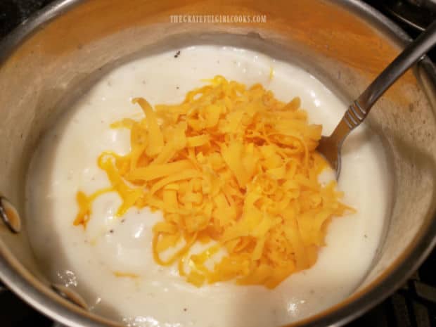 Grated cheddar cheese is stirred into the thickened white sauce in saucepan.