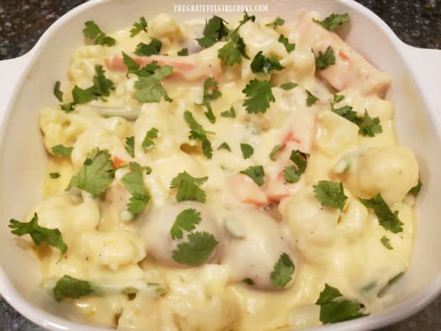 Chopped cilantro is sprinkled on top of the cheesy vegetable casserole before baking.