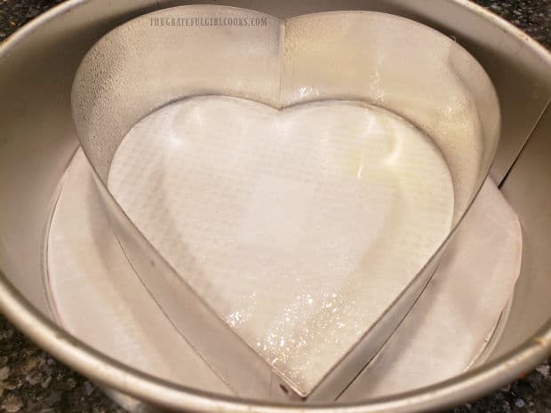 A heart shaped pan with removable bottom is placed inside a round springform pan. 
