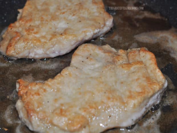 Golden brown pork chops pan-searing in a large skillet.