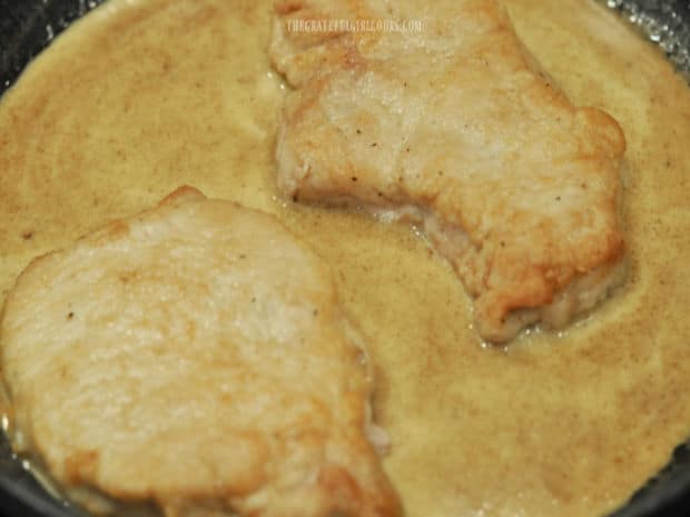 Pan-seared pork chops are added back into the skillet with creamy sauce and cooked.