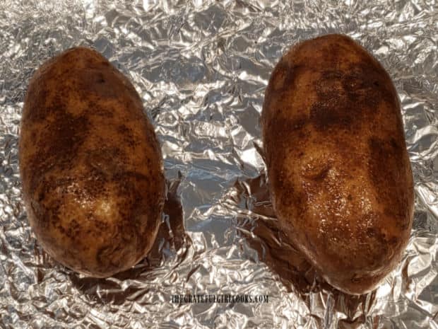 Two large russet potatoes are covered with oil before baking.