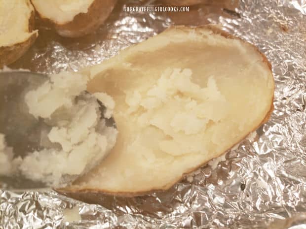 The baked potato insides are scooped out with a spoon, leaving a rim of potato intact.