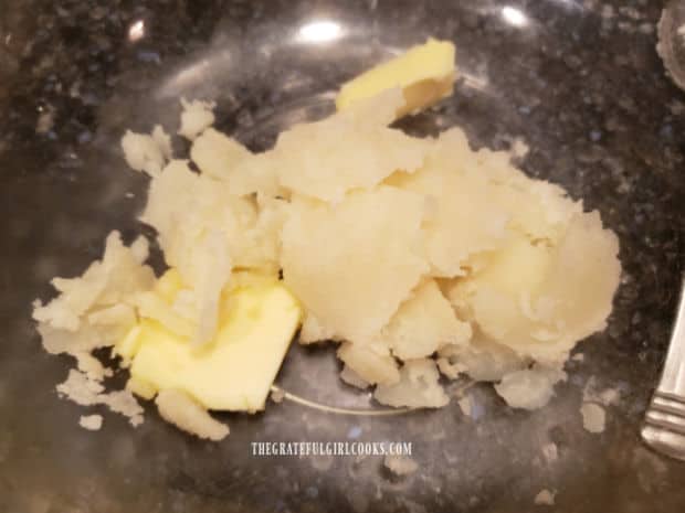 Hot, cooked potato is scooped onto butter in a large bowl, so the butter melts.