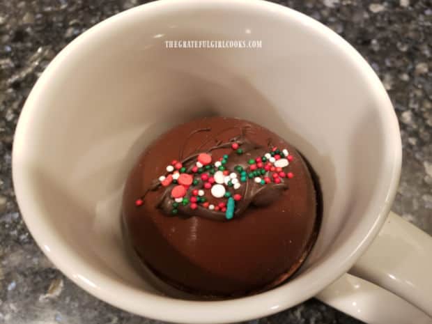 One of the hot cocoa bombs in a mug, waiting to be covered with hot milk or water.