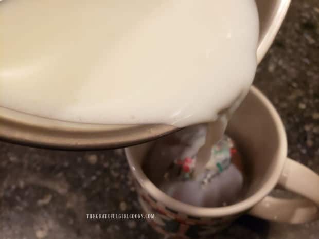 Hot milk is poured over one of the hot cocoa bombs in a large mug.