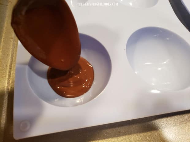 Melted chocolate wafers are placed into silicon half-sphere molds to coat the surface.