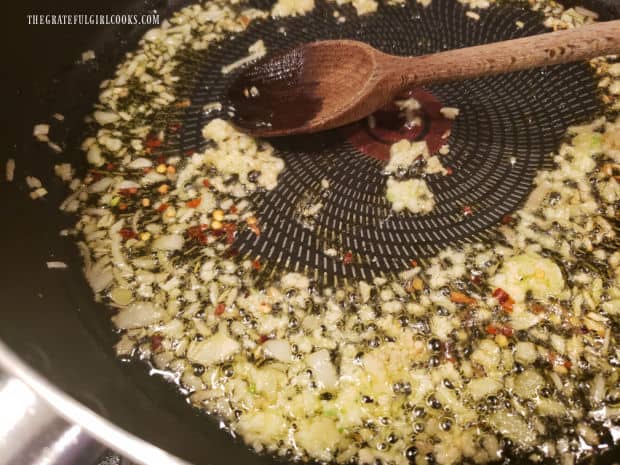 Garlic and red chili flakes are added to cooked shallots in skillet.