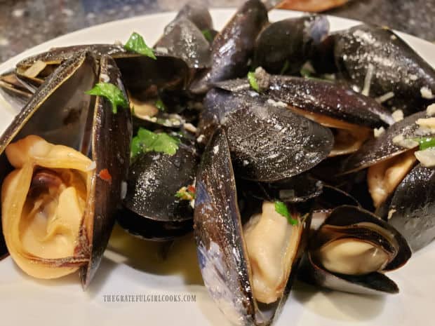 A bowl, full of the mussels in wine garlic butter sauce.