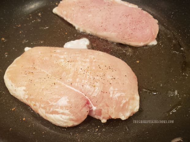 Lightly seasoned chicken breasts are pan-seared in hot oil in a skillet.