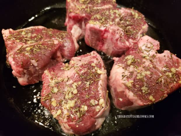 Seasoned lamb chops are pan-seared in oil in skillet.