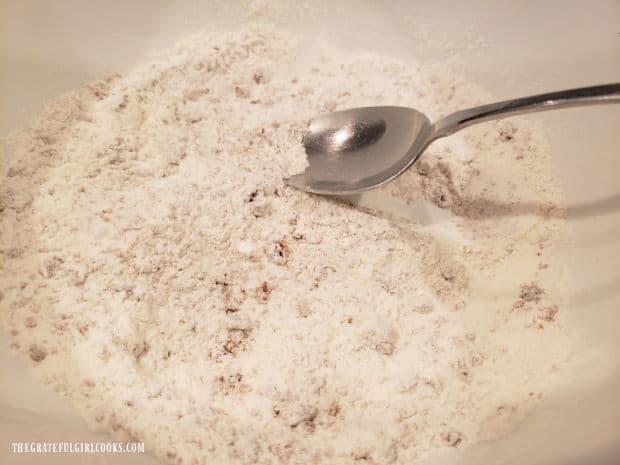 Flour and other dry ingredients are stirred together in a mixing bowl.