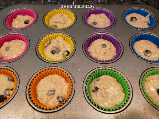 Muffin tin liners are filled with the thick blueberry batter before baking.