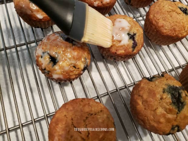 Powdered sugar glaze is painted onto the blueberry oat muffins with a pastry brush.