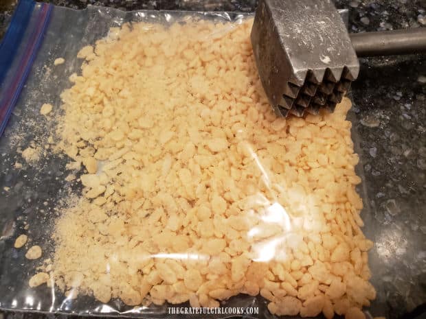 Puffed rice cereal in plastic bag is crushed using the flat side of a meat mallet.