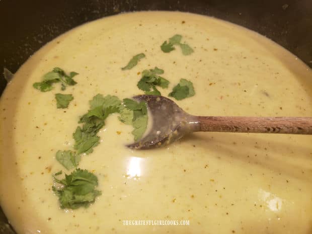 Cilantro leaves are added to the green curry sauce in the skillet.