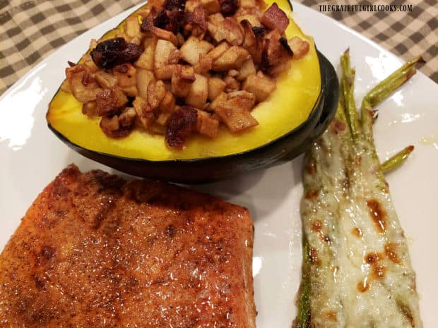 The apple pecan stuffed acorn squash, shown served with asparagus and salmon on plate.