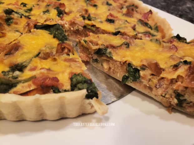 A slice of the bacon, onion and spinach tart is removed from the pan, for serving.
