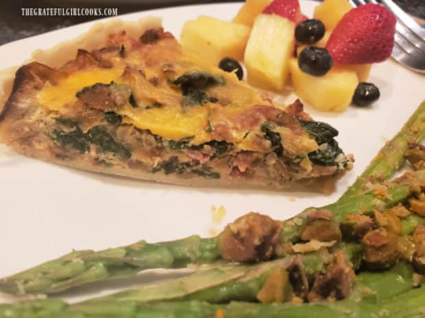 Asparagus and fresh fruit are served alongside a slice of bacon, onion and spinach tart.