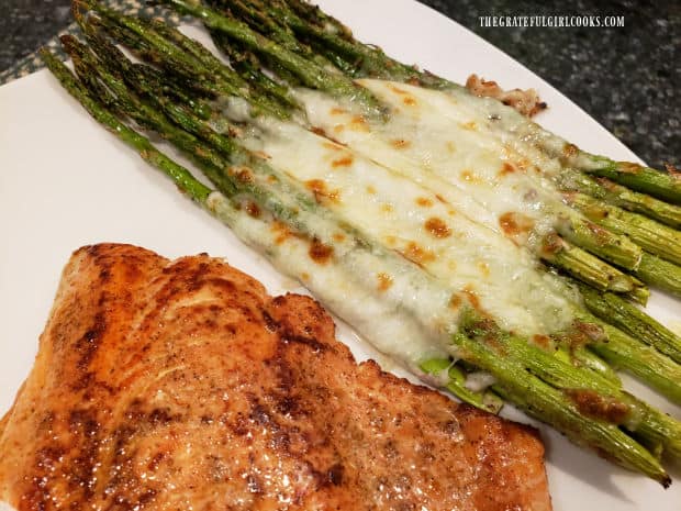 A portion of the cheesy garlic roasted asparagus is served alongside salmon on plate.