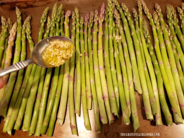 A garlic and olive oil mixture is drizzled over fresh asparagus before baking.