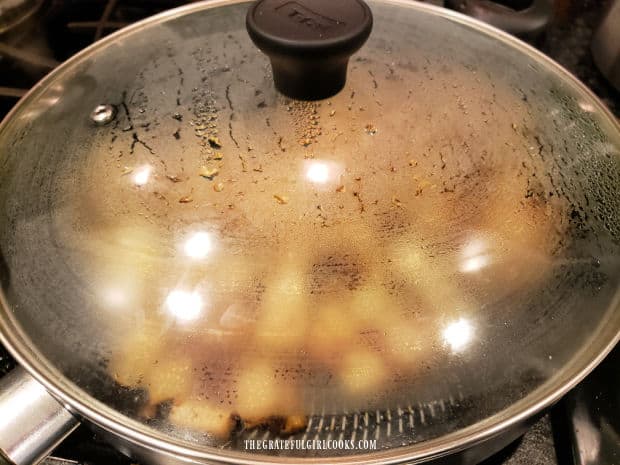 A lid covers the pan of country skillet potatoes to steam them until tender.