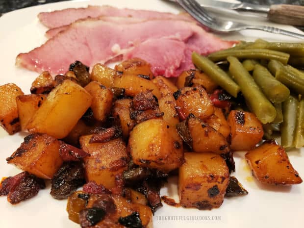 A serving of country skillet potatoes, served with ham slices and green beans.