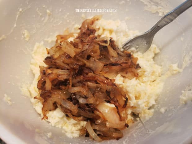 Caramelized onions are stirred into the dip mixture in the bowl.
