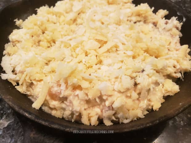 Dip is spread in a cast iron skillet and topped with shredded cheeses.