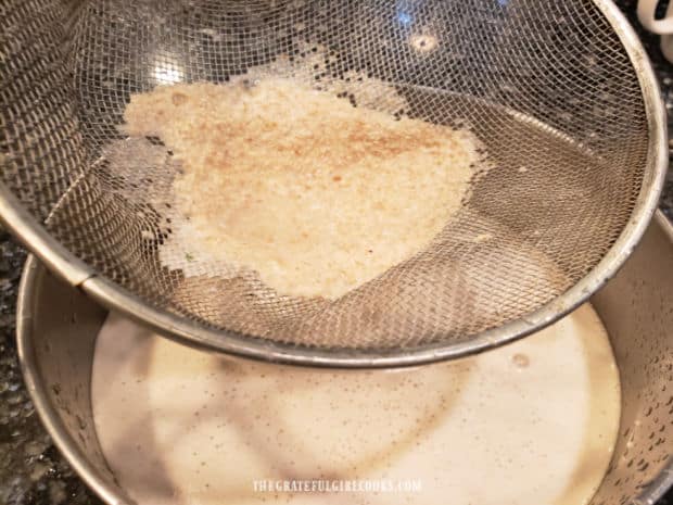 Oat milk is poured through a fine mesh strainer into bowl, leaving pulp in strainer.