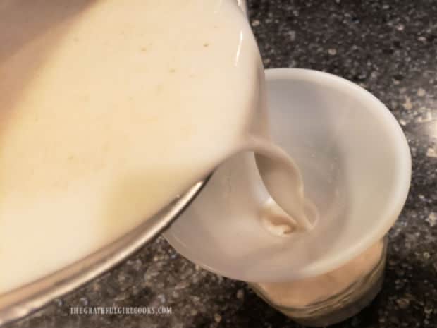 A funnel is inserted in a jar and oat milk is poured into the jar through the funnel.