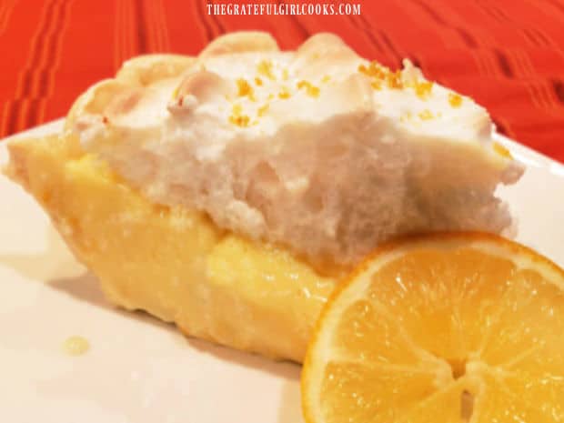 A slice of the sour cream lemon meringue pie on a plate with a lemon slice garnish.