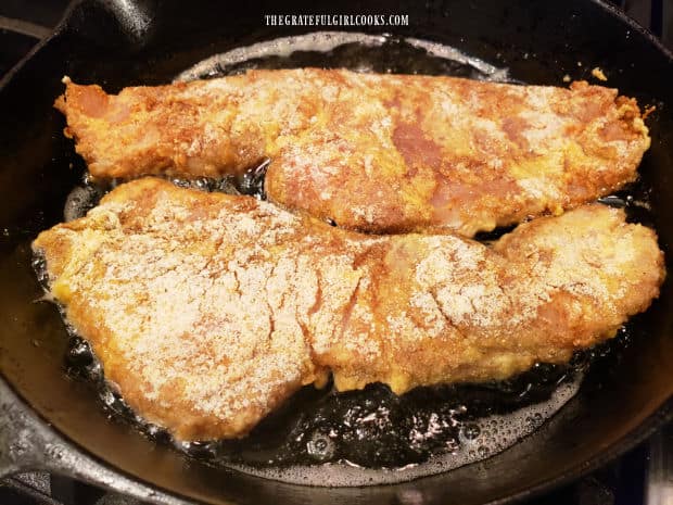 Seasoned rockfish fillets are fried in a large skillet in very hot oil.