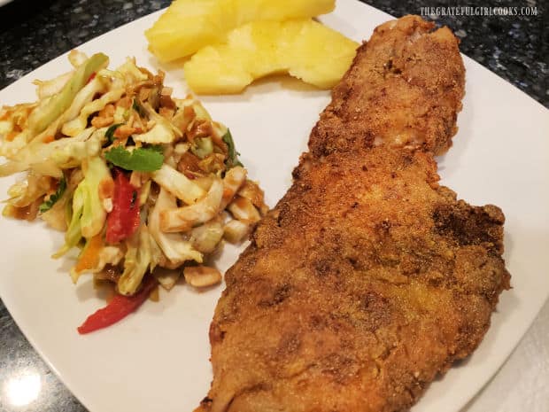 A white plate with coleslaw, pineapple, and a piece of Southwestern fried rockfish.