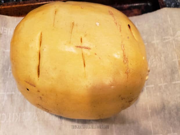 A spaghetti squash is pierced several times with a knife before roasting in the oven.