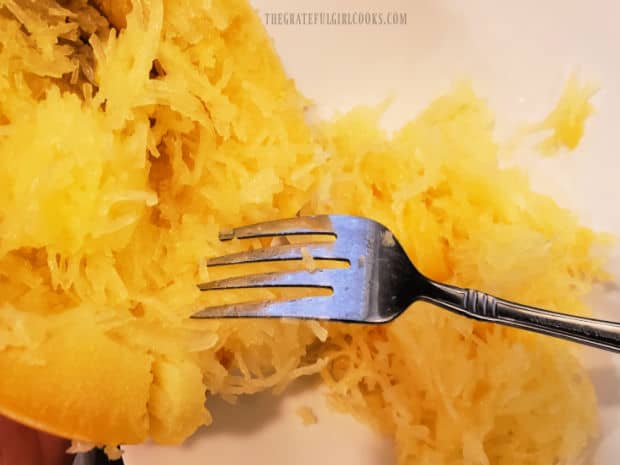 A fork is used to pull long strands of spaghetti squash away from the squash peel.