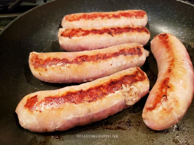 Italian sausages are cooked through by pan-searing them in a skillet with oil.
