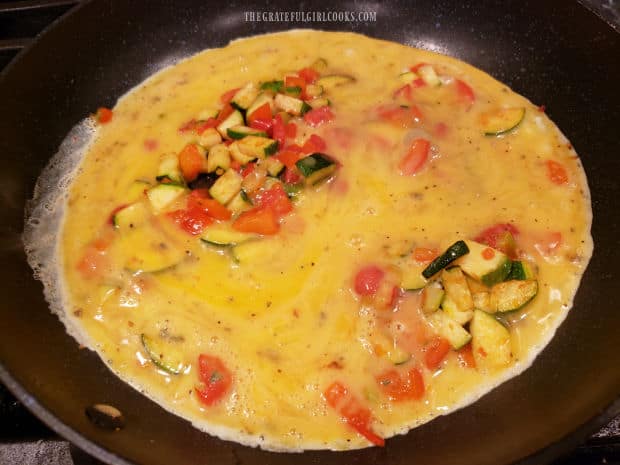 Beaten, seasoned eggs are added to the cooked veggies in the skillet to cook.
