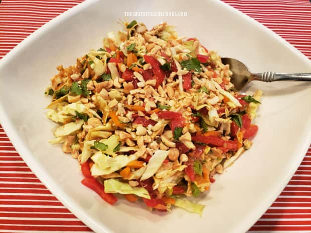 Thai coleslaw in peanut sauce is garnished with chopped peanuts, and served in a white dish.