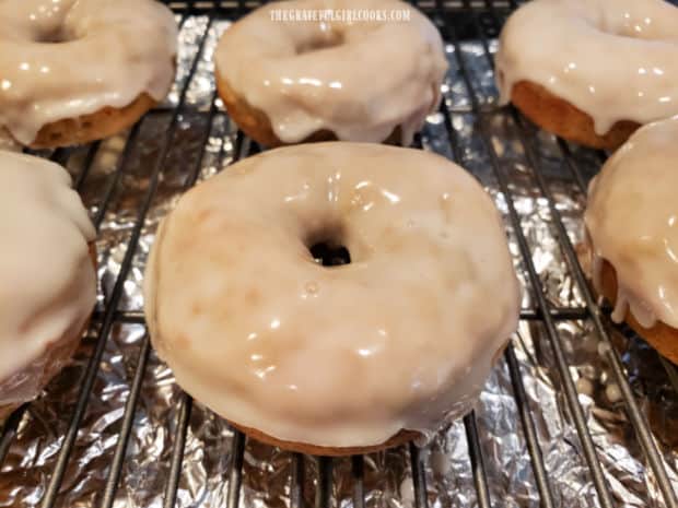 Six baked banana doughnuts on a wire rack after being glazed.